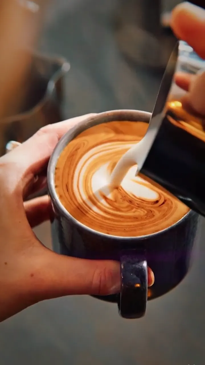 Latte art being poured into a dark mug